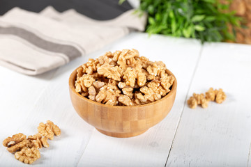 Walnut kernels in a wooden bowl on white background.