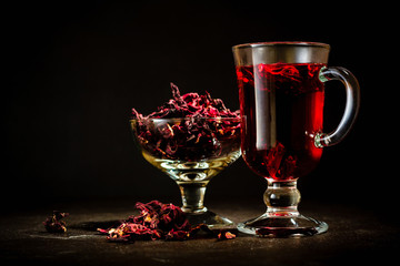 Transparent glass Cup with hot red tea from hibiscus or hibiscus. Glassware and dry petals with...