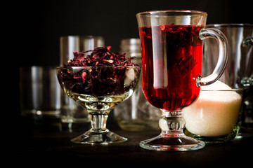 Transparent glass Cup with hot red tea from hibiscus or hibiscus. Glassware and dry petals with sugar.