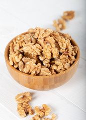 Walnut kernels in a wooden bowl on white background.
