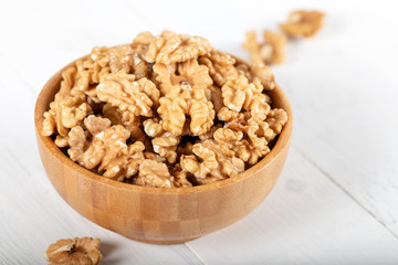 Walnut kernels in a wooden bowl on white background.