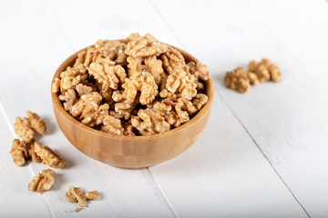 Walnut kernels in a wooden bowl on white background.