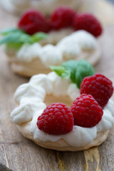 Mini Pavlova dessert with raspberries and mint. Served on a wooden board, high resolution