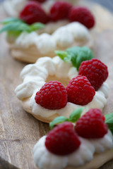 Mini Pavlova dessert with raspberries and mint. Served on a wooden board, high resolution
