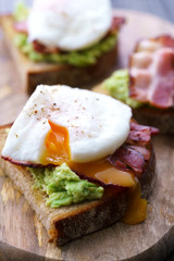Poached egg toasts with avocado and bacon. Served on a wooden board, high resolution