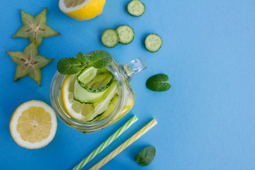 Detox or infused water with cucumber, carambola and lemon on the blue background.Top view.Copy...