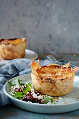 Potato gratin baked in filo dough, with crispy cheese crust and with a salad of arugula, sun-dried tomatoes and cheese on a blue background. A dish of french cuisine