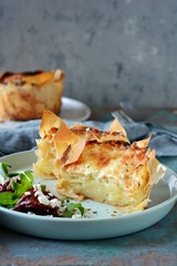 Potato gratin baked in filo dough, with crispy cheese crust and with a salad of arugula, sun-dried tomatoes and cheese on a blue background. A dish of french cuisine