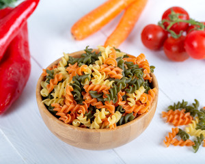 Colorful raw rotini pasta with vegetables on white background