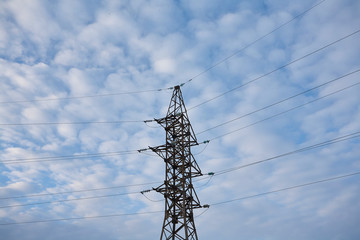 Metal support for high-voltage wires against the sky with clouds.