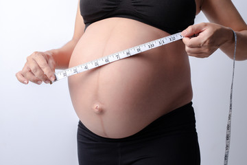 Pregnant women wear black shirts. who measured her stomach with a tape measure on a white background