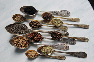 Spices, seeds, herbs in vintage silver spoons on wooden background