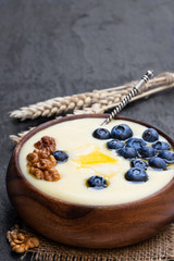 Wooden bowl of semolina porridge with blueberry and walnut on black stone background