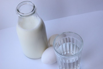 Milk bottle, water glass, eggs on white background