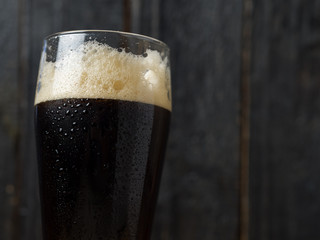 A glass of dark beer with copyspace on a wooden background