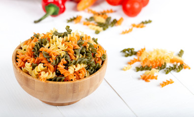 Colorful raw rotini pasta with vegetables on white background