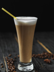 An elongated beautiful glass of latte coffee with a straw