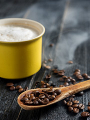 Yellow cappuccino coffee mug and coffee beans in wooden spoon