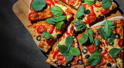 Pizza with Mozzarella cheese, Tomatoes, pepper, olive, Spices and Fresh spinach. Italian pizza. Pizza Margherita or Margarita on Dark grey black slate background
