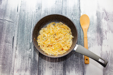 Fried onions in a pan. Kitchen spatula. Beautiful wooden background.
