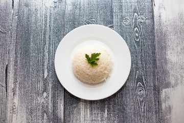 boiled rice in a white plate. wooden background. parsley