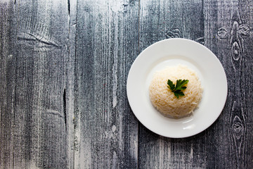 boiled rice in a white plate. wooden background. parsley