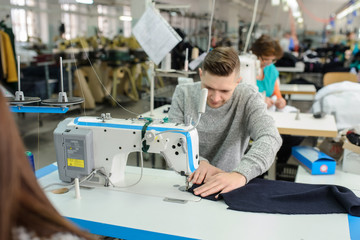 close up photo of a young man sewing with sewing machine in a factory