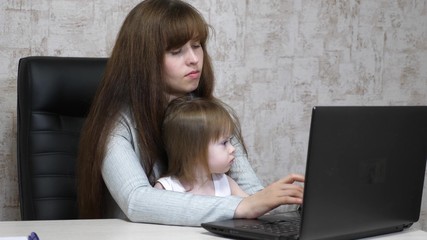 Working mother with her little daughter at table. Busy woman working on laptop with baby on hands. Working mom with beautiful infant on hands in cozy home. Female freelance work. Modern motherhood