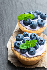 Mini tarts with blue cream and fresh blueberries on black stone background