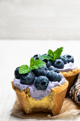 Mini tarts with blue cream and fresh blueberries on white wooden table