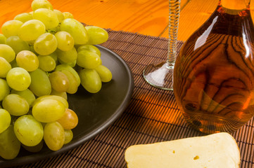 large brush of green grapes in a ceramic plate, a decanter and a glass of wine and cheese