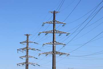 Power line supports with electrical wires on clear blue sky background. High voltage electricity transmission lines, power supply concept