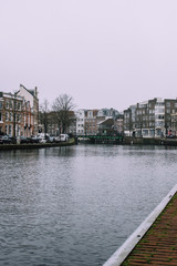 Obraz premium Beautiful cityscape in Haarlem, Netherlands. Tiny waves on the river, bridge, and dark bricked houses on the both sides of the canal. Cold cloudy weather.