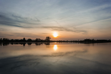 Fototapeta na wymiar Sunset behind a foggy sky over a calm lake