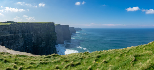 Vue panoramique d'une succession de falaises d'Irlande avec de l'herbe verte en premier plan