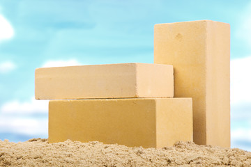 Three yellow ceramic bricks on the sand at the blue sky background