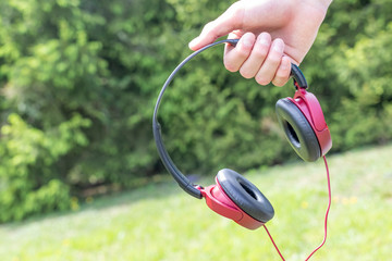 Naklejka premium Red-black headphones in hand on the background of coniferous trees in the park.