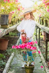 Foto op Canvas Little girl helps watering plants and gardening in greenhouse © svittlana