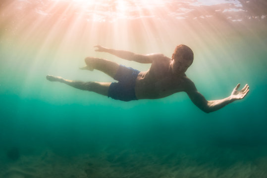 Man suspended above sandy lake bottom in sunlight dappled murky