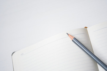 Notebook with pencil on white wooden table.