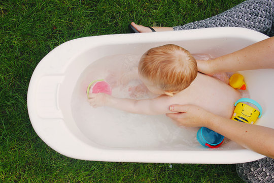 A baby girl is taking a bath outside in the warm summer air
