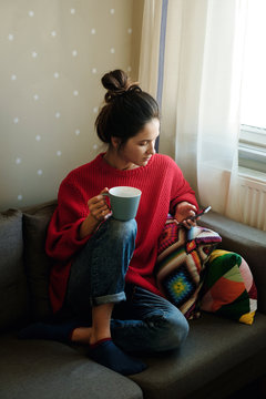 Young woman interact with her smartphone while drink coffee in the living room