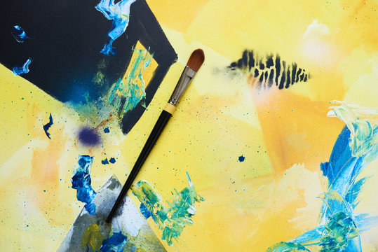 Close-up of paintbrush on colorful painted canvas.