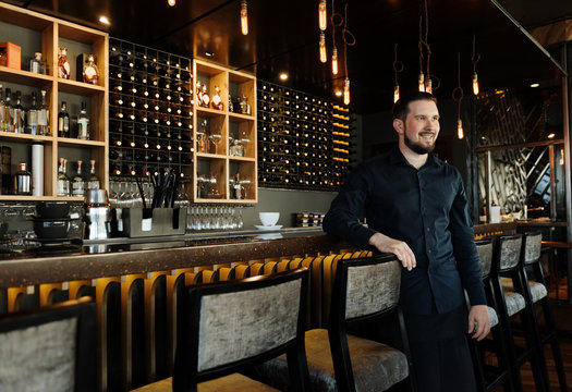 Cheerful barista in black near counter