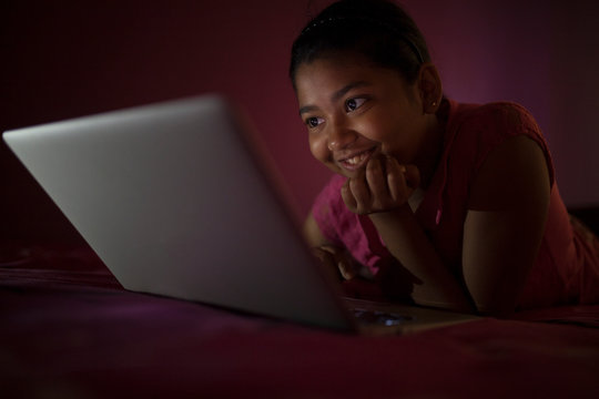 Teenage Girl Lying On The Bed Comfortably And Using Laptop Inside A Room