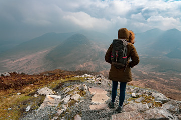 une femme de dos avec sa capuche et son sac à dos au sommet d'une montagne