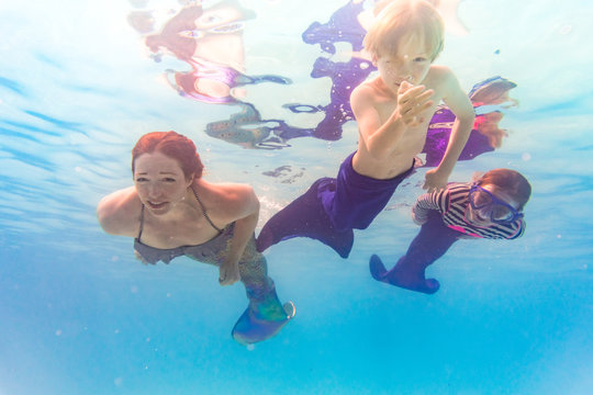 Family on Florida vacation has fun swimming in pool together using mermaid tail monofins