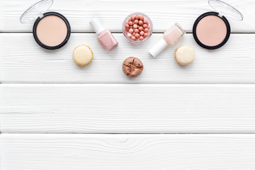 Make-up artist desk with powder, decorative cosmetics and macaroon cookies on white wooden background top view mokeup