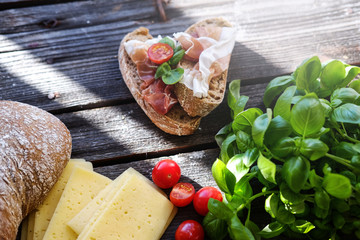 Small sandwiches with meat, cherry tomatoes, cheese, bread and basil on the black table.