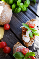 Small sandwiches with meat, cherry tomatoes, cheese, bread and basil on the black table.